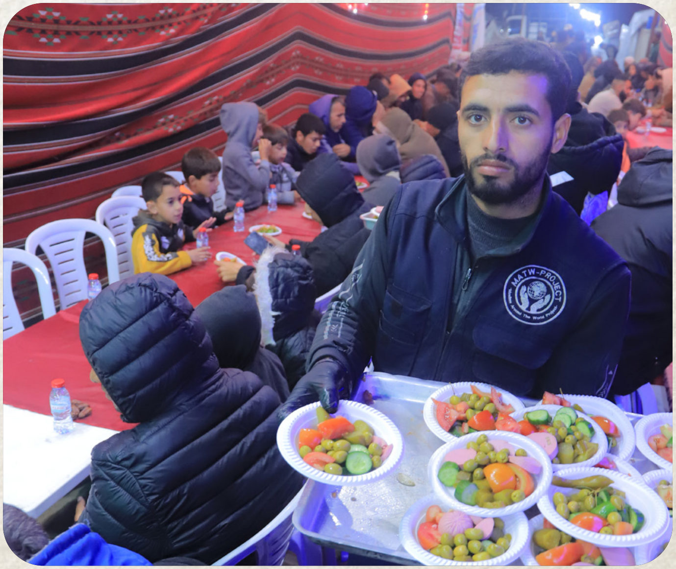 A Najam worker carrying trays of hot meals toward waiting families in Gaza