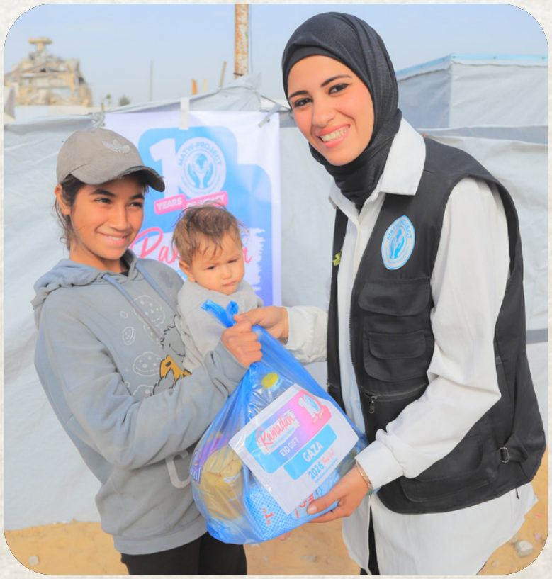 A Najam team member handing an Eid gift to a child held by her mother